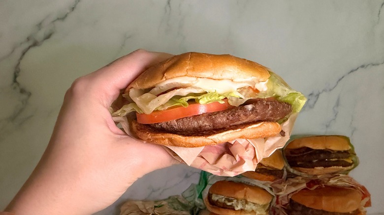 Hand holding Jumbo Jack burger from Jack in the Box against marble surface background.
