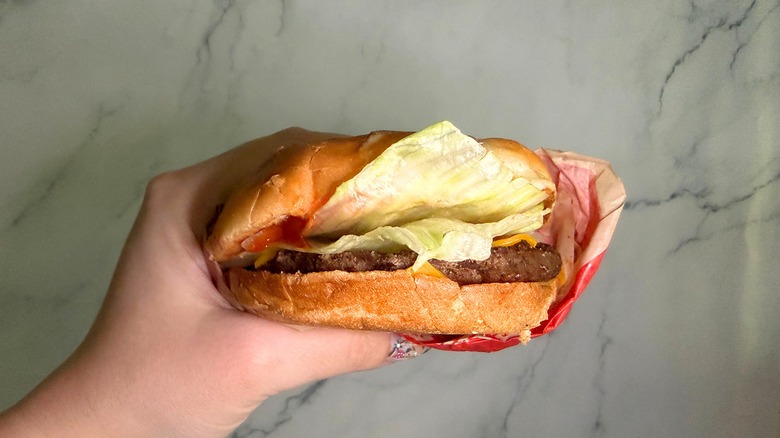 Hand holding Jumbo Jack Cheeseburger from Jack in the Box with marble surface in background