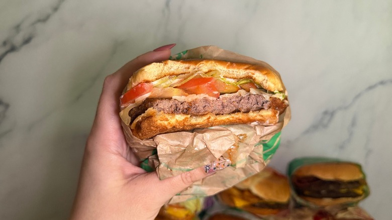 Hand holding burger with bite taken out of it on marble background