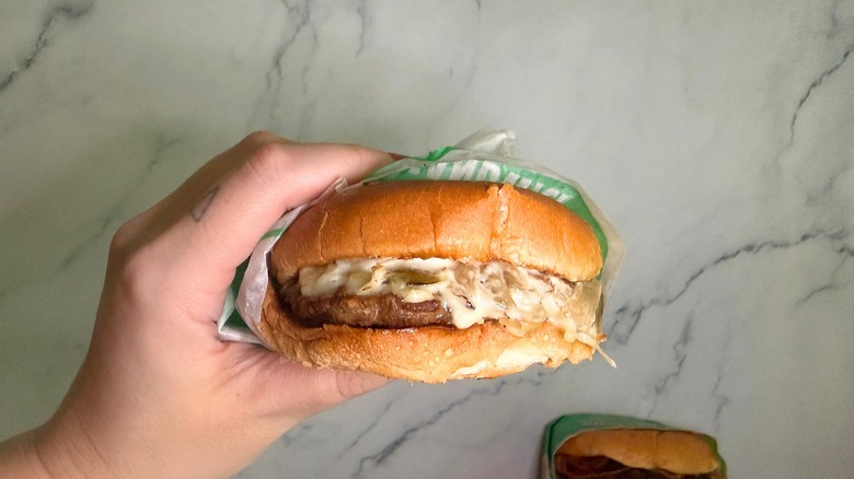 Hand holding Philly-style bonus Jack burger from Jack in the Box, burgers on marble surface in background