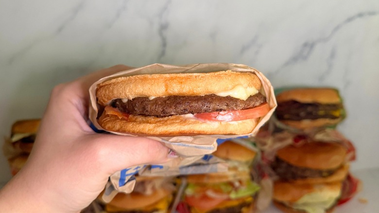 Hand holding Sourdough Jack burger from Jack in the Box, burgers on marble surface in background