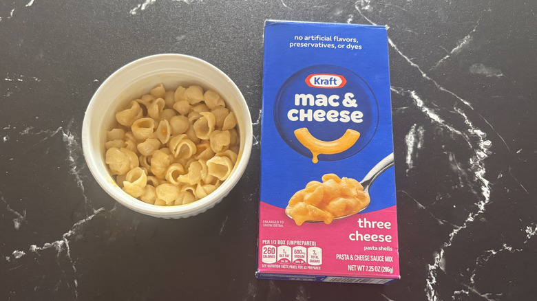 Kraft three cheese mac and cheese box next to bowl of mac and cheese shells