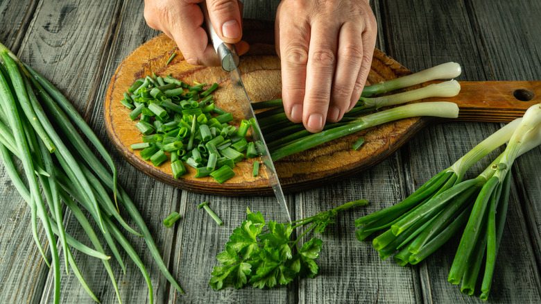 Person cutting up green onion on cutting board
