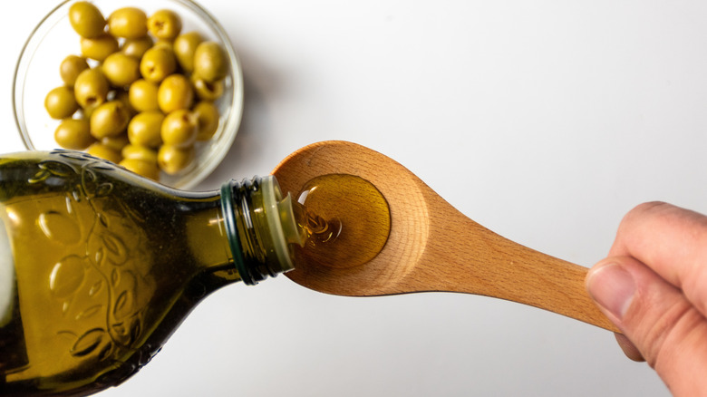 Extra virgin olive oil being poured onto spoon with olives in the background