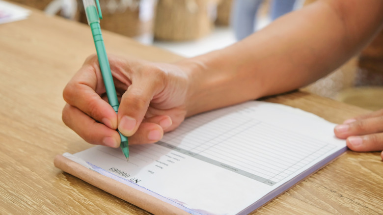 Person's hand writing a check on wooden table