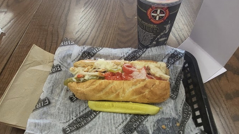 A Firehouse Subs Smokin' Honey Chicken Melt in a paper-lined tray next to a pickle spear