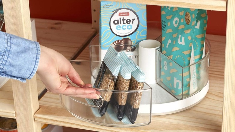 A woman reaching towards a plastic Lazy Susan holding snacks in a pantry