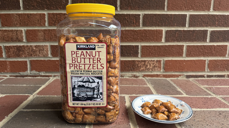 Tall plastic container of Kirkland Signature peanut butter-filled pretzels on brick surface, with some displayed on adjacent plate