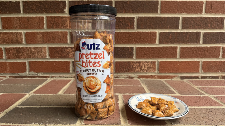 Tall plastic container of Utz peanut butter-filled pretzels on brick surface, with some displayed on adjacent plate