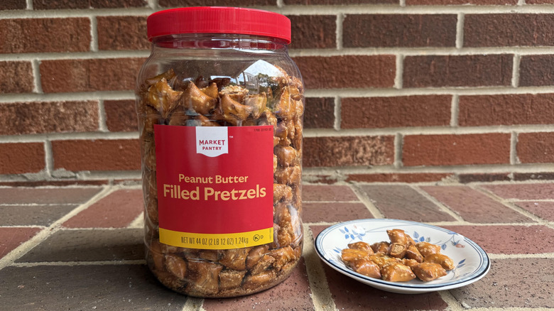 Tall plastic container of Market Pantry peanut butter-filled pretzels on brick surface, with some displayed on adjacent plate
