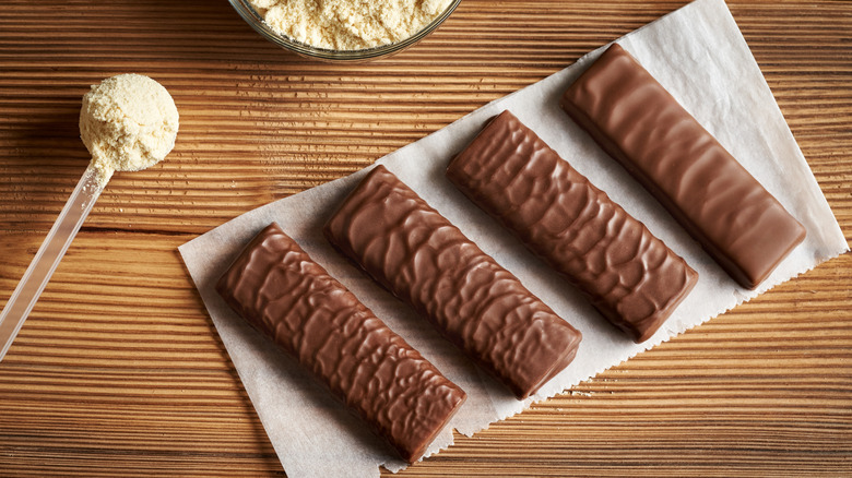 Chocolate-covered protein bars next to a scoop of protein powder