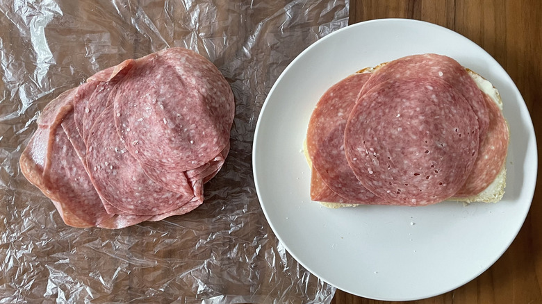 Hard salami on a plastic sheet and an open sandwich