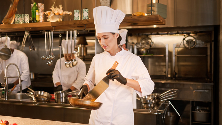Chef in a kitchen working with a hot pan of food