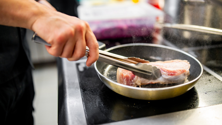 Chef cooking meat in a stove-top pan