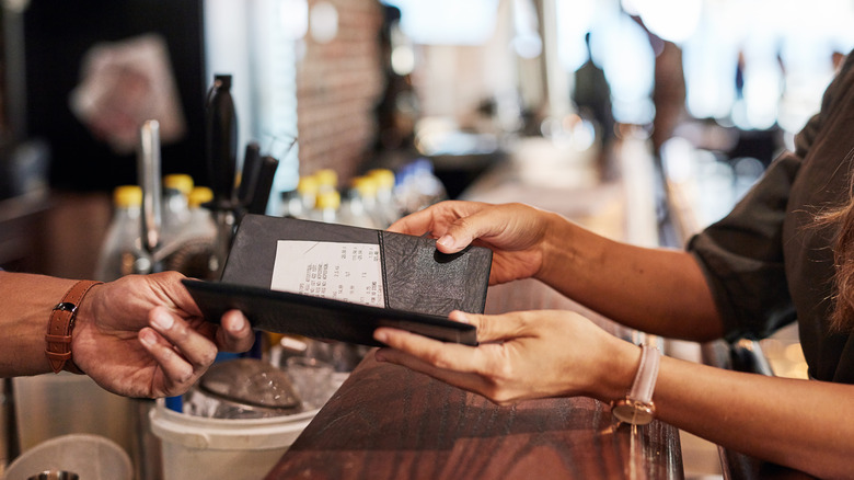 Server hands customer check to their manager