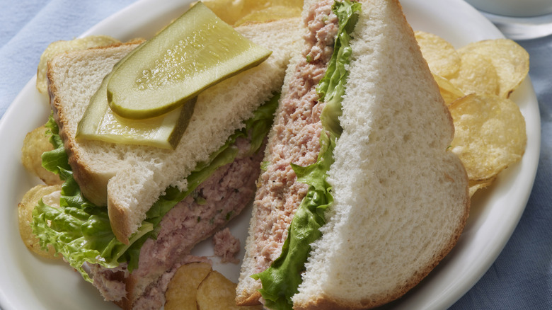 A deviled ham sandwich topped with pickles, accompanied by potato chips