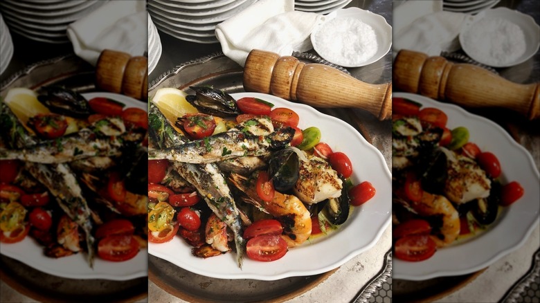 Rustic-looking dish of sardines and vegetables with a pepper shaker