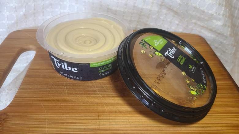 Open tub of Tribe's hummus on wooden cutting board