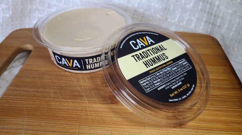 Open tub of Cava hummus on wooden cutting board