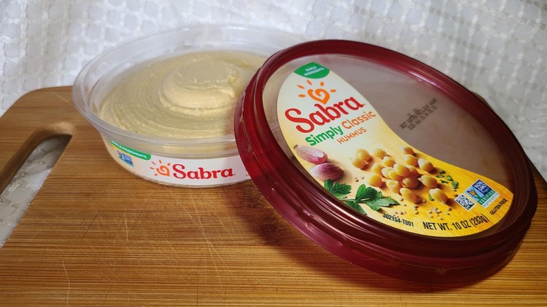 Open tub of Sabra hummus on wooden cutting board