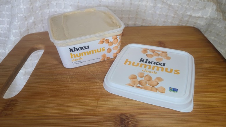 Open tub of Ithaca hummus on wooden cutting board