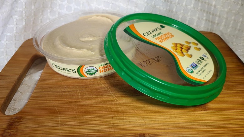 Open tub of Cedar's hummus on wooden cutting board