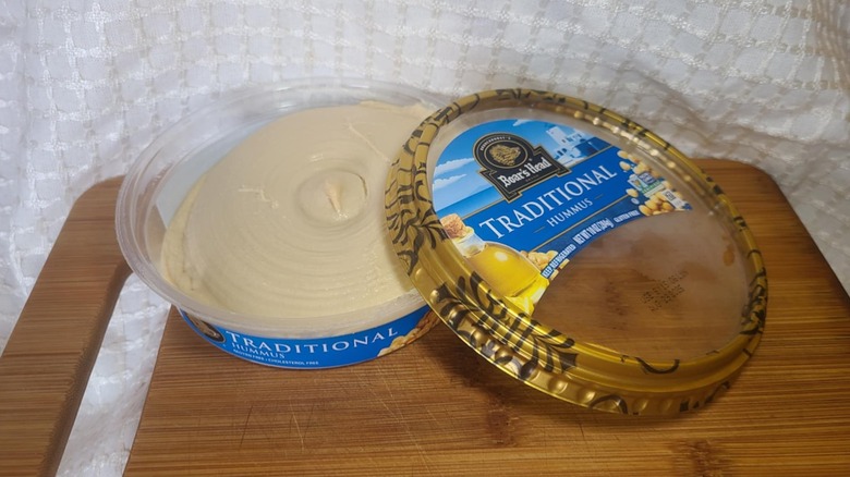Open tub of Boar's Head's hummus on wooden cutting board