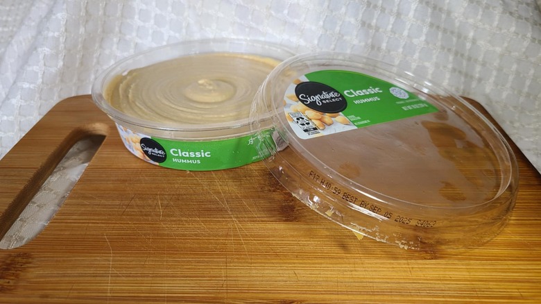 Open tub of Safeway's hummus on wooden cutting board