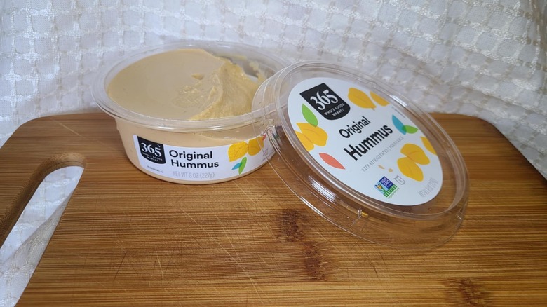 Open tub of Whole Food's hummus on wooden cutting board