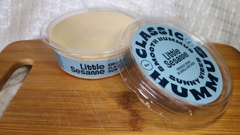 Open tub of Little Sesame's hummus on wooden cutting board
