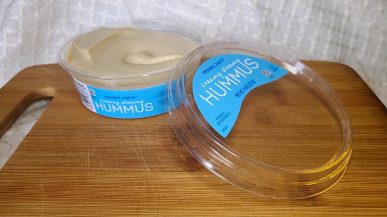 Open tub of Trader Joe's hummus on wooden cutting board