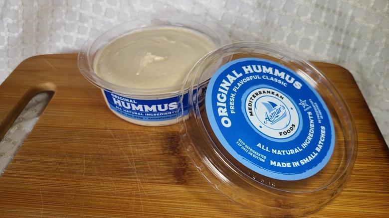 Open tub of Asmar's hummus on wooden cutting board