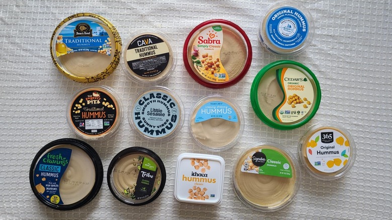 Overhead shot of 13 brands of hummus on white background