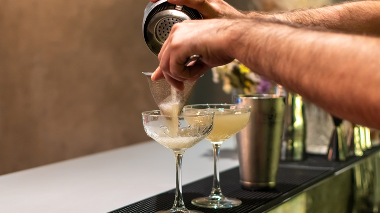 A bartender is pouring a cocktail through a strainer
