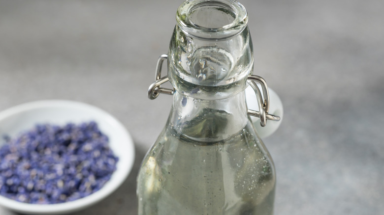 The top of a bottle of clear syrup with lavendar in the background