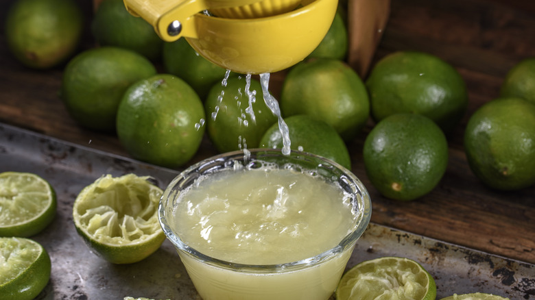 Lime juice getting squeezed out of fresh limes with many whole and cut limes around