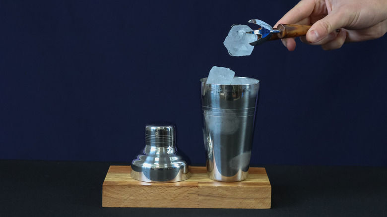 Someone adding an ice cube into a cocktail shaker