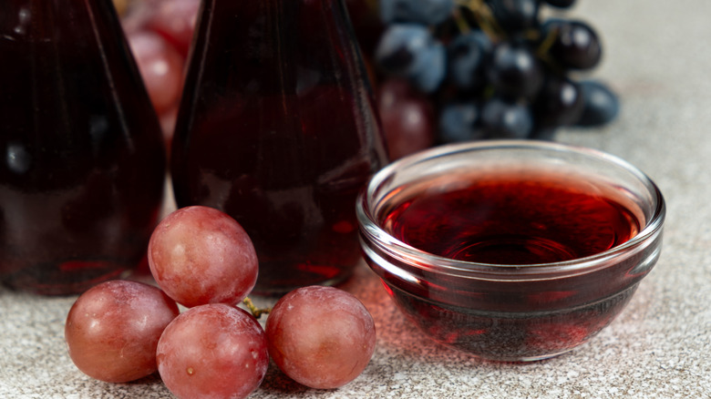 Red wine vinegar in small glass bowl next to fresh red grapes