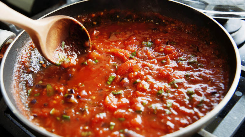 Pasta sauce cooking in pan and being stirred by wooden spoon