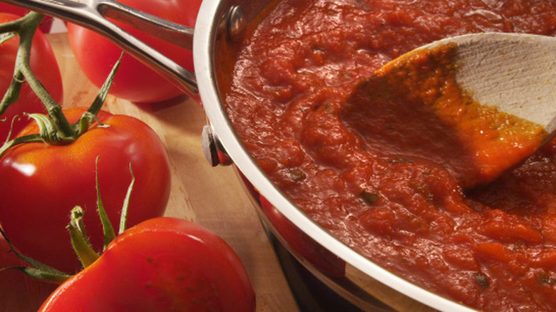 Pasta sauce cooking in pan with wooden spoon and fresh tomatoes