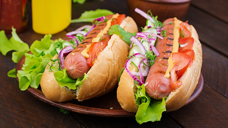 Two hot dogs in buns with lettuce, onion, tomato, and light orange sauce sitting on brown plate