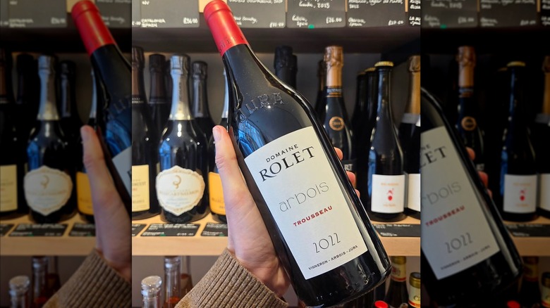 Hand holding Domaine Rolet Arbois Trousseau red wine bottle