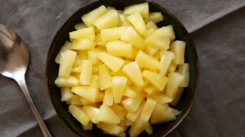 Canned pineapple chunks in brown bowl next to spoon