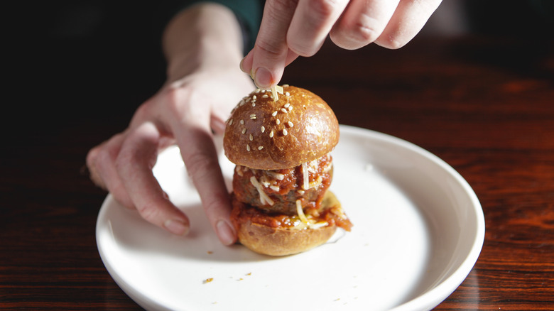 Hand holding mini meatball slider on white plate