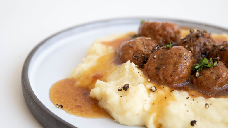 Meatballs and gravy on mashed potatoes on white plate