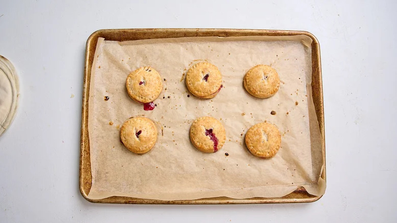Six cherry hand pies on a baking sheet.