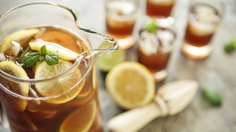 Pitcher of sweet tea with lemons and mint, glasses of sweet tea in the background.
