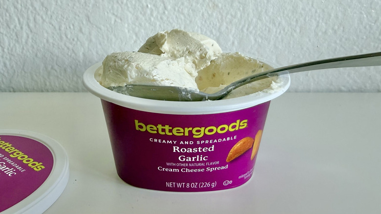 Container of bettergoods Roasted Garlic Cream Cheese Spread with some of it scooped on a spoon
