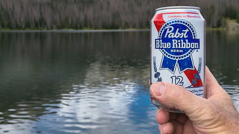 Hand holding can of PBR in front of lake background