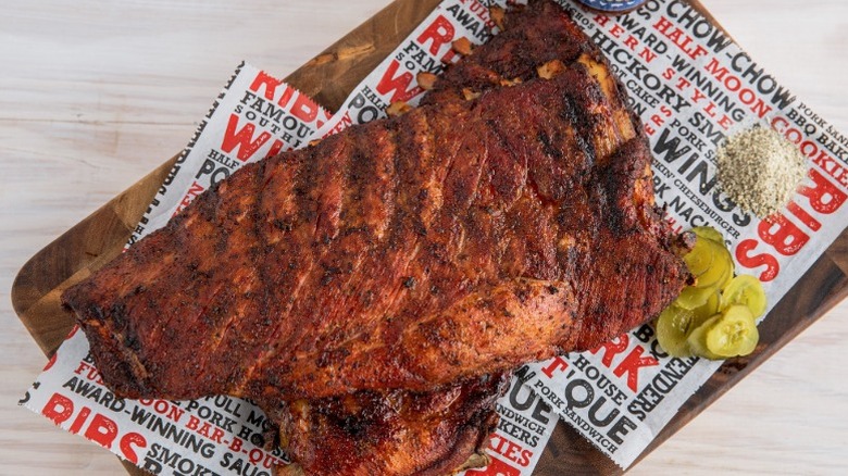 two racks of smoked barbecue ribs with pickles on cutting board